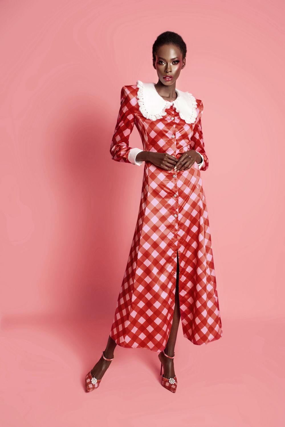 Langes kariertes Kleid mit Knopfleiste, weißen Manschetten und Kragen, getragen von einem Model vor rosa Hintergrund.