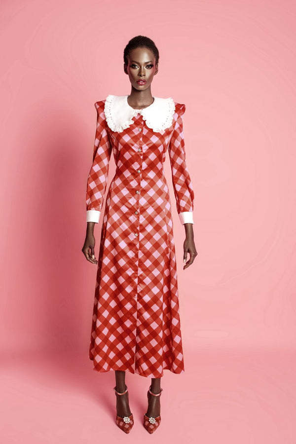 Langes kariertes Kleid mit Knopfleiste, weißen Manschetten und Kragen, getragen von einem Model vor rosa Hintergrund.