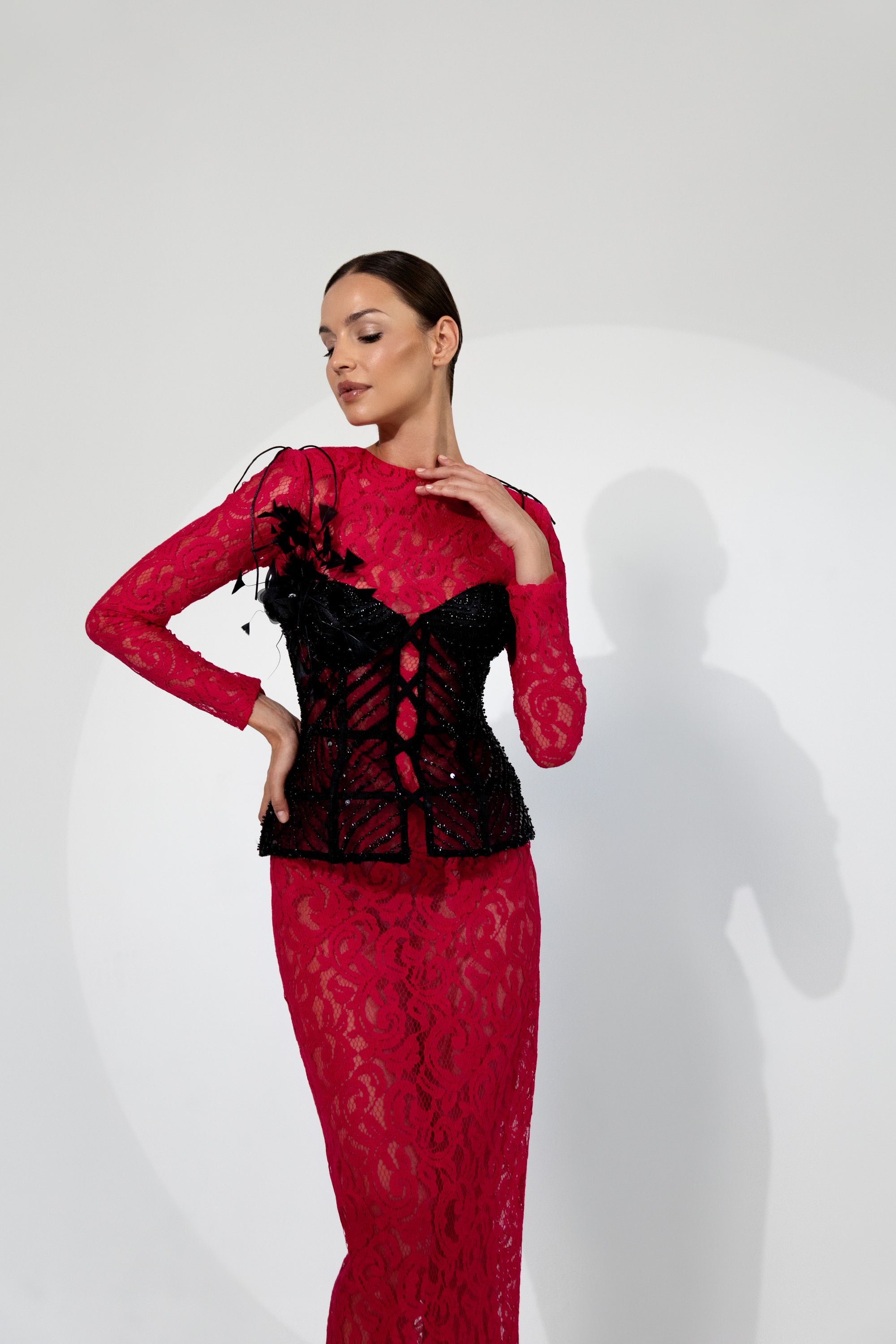 Frau in einem roten, figurbetonten Spitzenkleid mit langen Ärmeln, kombiniert mit einem schwarzen, bestickten Korsett.